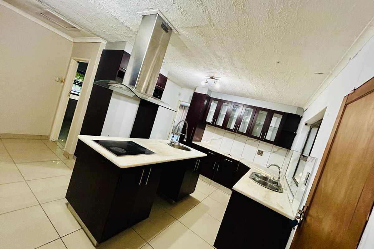 A spacious kitchen featuring dark cabinetry, a central island with a built-in hob, stone countertops, and tiled flooring.
