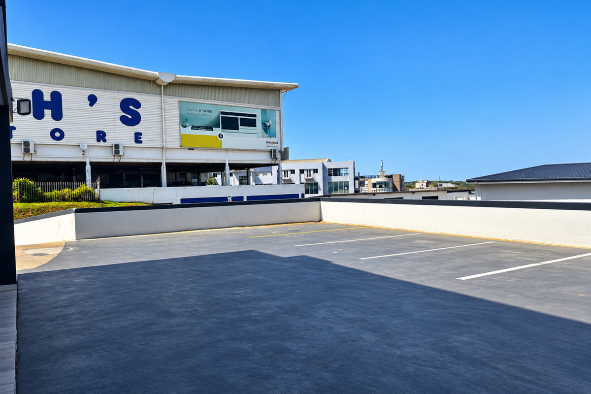 An open-air paved parking area with marked bays and a perimeter wall, situated adjacent to a commercial building.