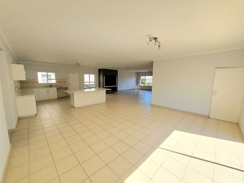 Spacious open-plan living area featuring a functional kitchen with island, tiled flooring throughout, and a prominent built-in fireplace.