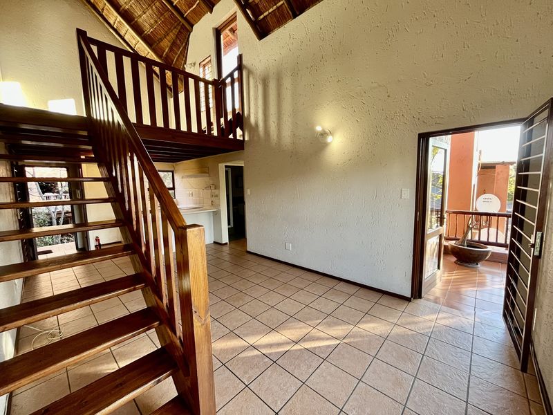Open-plan living area featuring a wooden staircase leading to a mezzanine level, tiled flooring, and direct access to a private balcony.