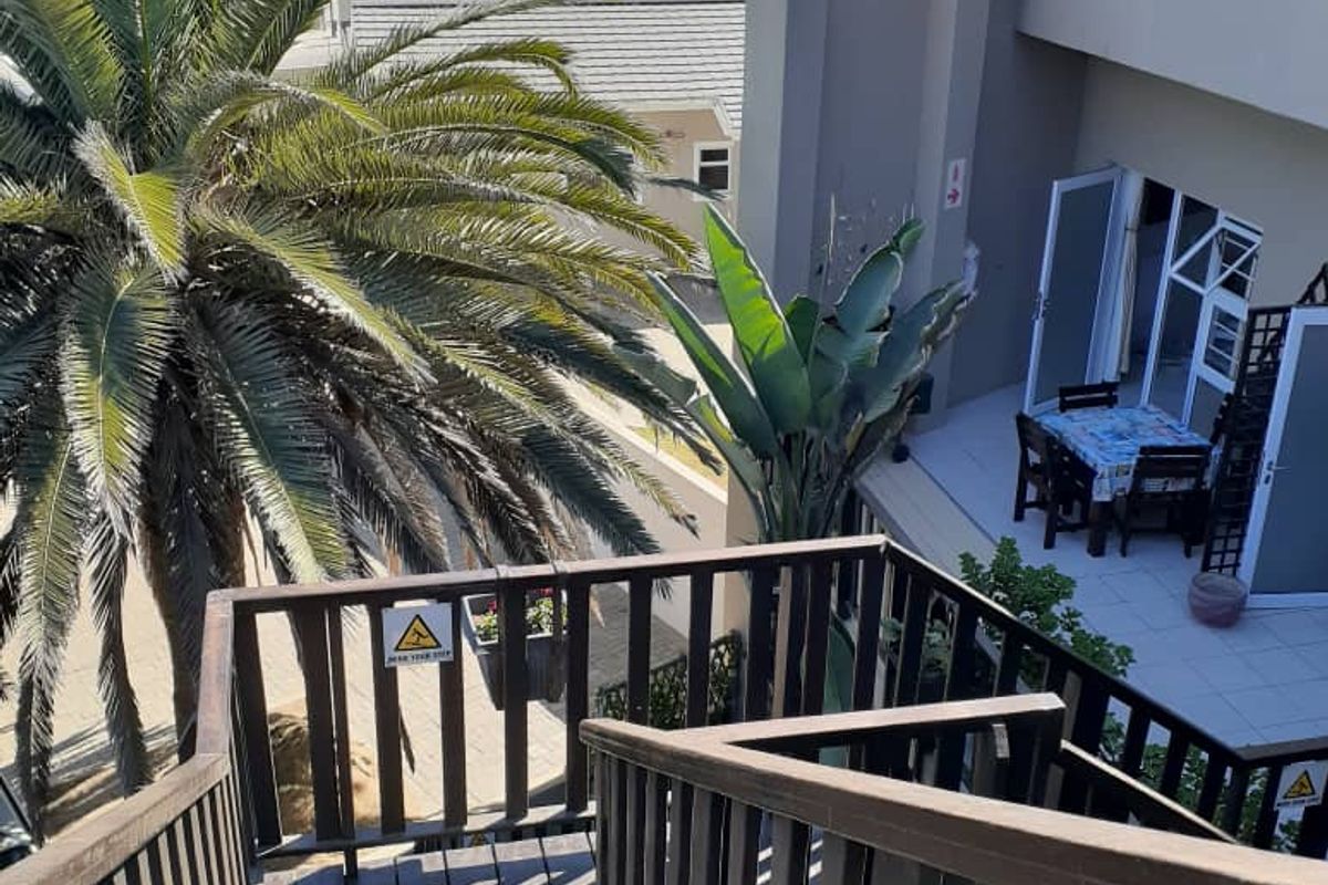 An elevated view of a wooden staircase leading down to a tiled patio area with sliding glass door access.