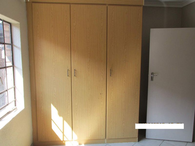 A bedroom featuring a large built-in wooden wardrobe, tiled flooring, and a window with security bars.