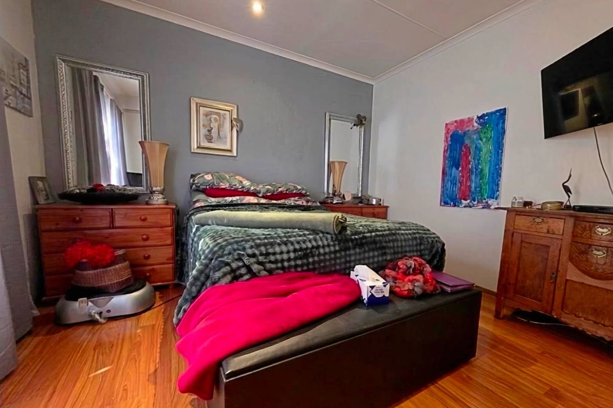 A bedroom featuring timber flooring, a feature wall, and recessed downlighting.