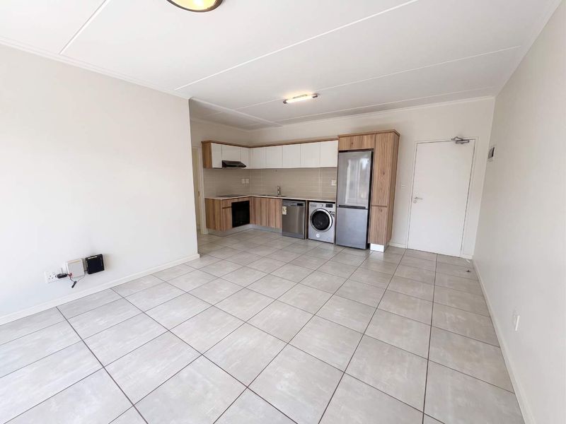 An open-plan kitchen and living area featuring modern wood-finish cabinetry, tiled flooring, and integrated appliances in a clean, neutral space.