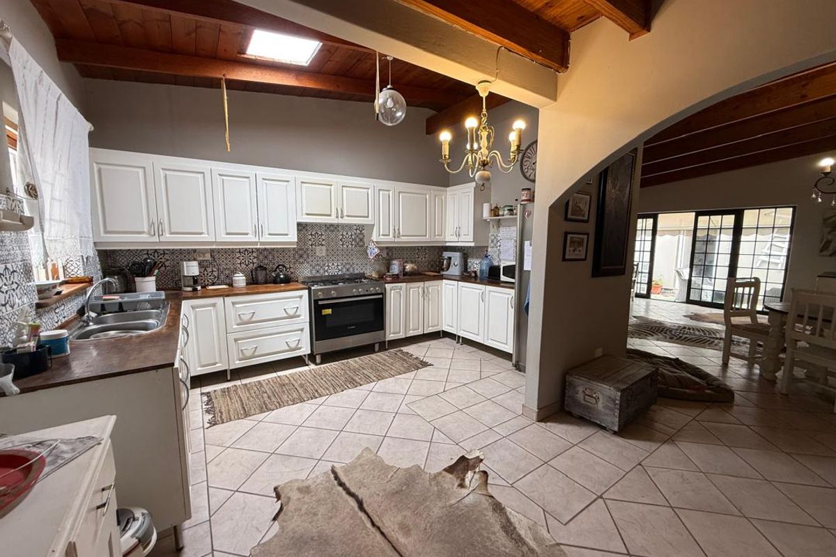 Spacious kitchen featuring white cabinetry, wooden countertops, patterned tile backsplash, exposed timber ceiling beams, and a skylight, flowing into an adjacent living area.