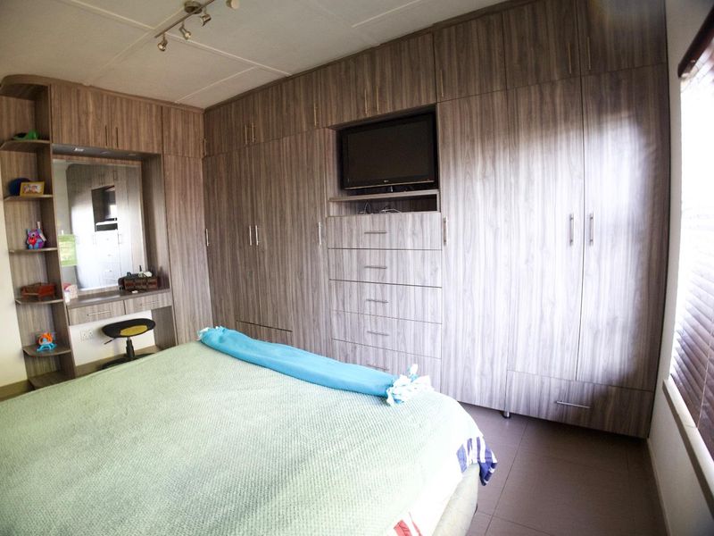 A well-appointed bedroom featuring extensive built-in cabinetry with integrated vanity and storage, tiled flooring, and venetian blinds for light control.