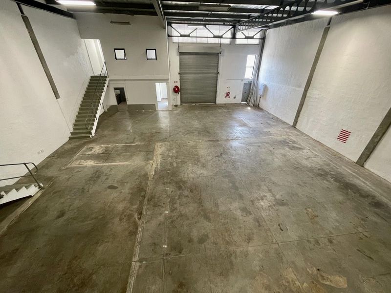 Spacious industrial warehouse unit featuring high ceilings, exposed steel trusses, a large roller shutter door, and concrete flooring, suitable for various commercial or storage uses.