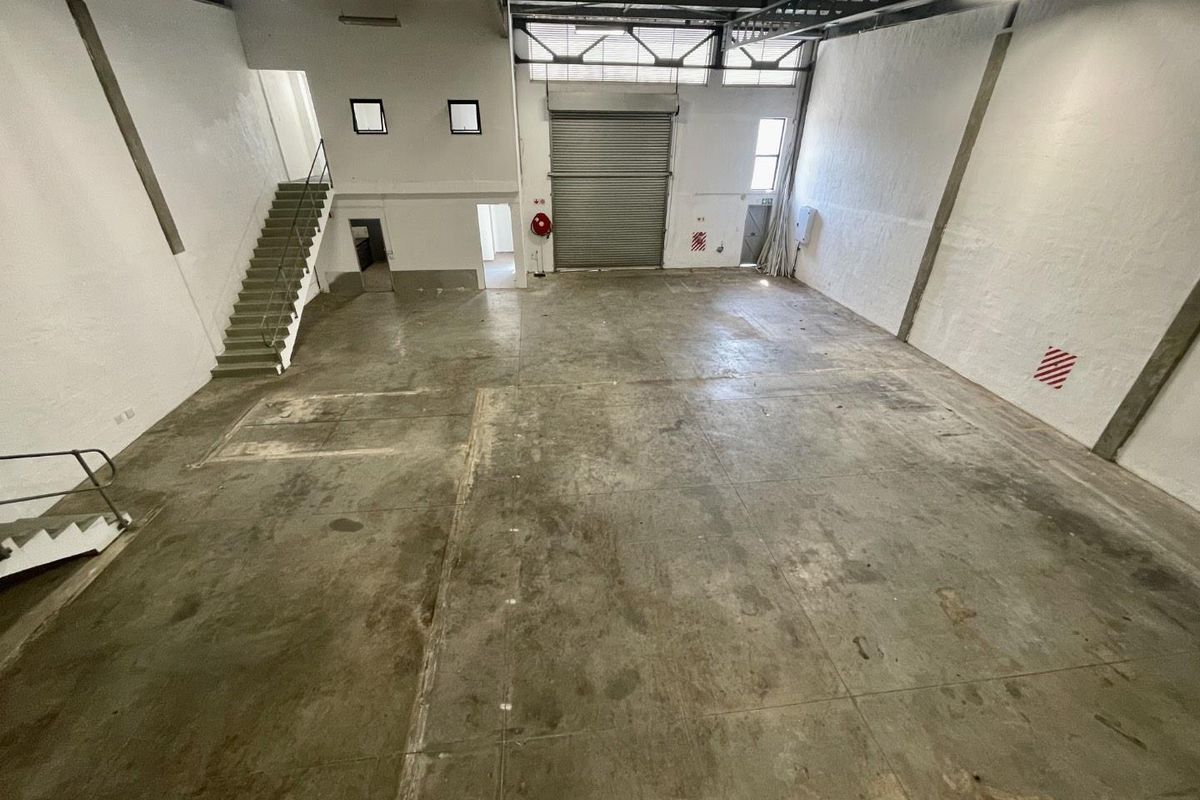 Spacious industrial warehouse unit featuring high ceilings, exposed steel trusses, a large roller shutter door, and concrete flooring, suitable for various commercial or storage uses.