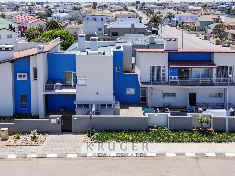Aerial view of a modern multi-level residential property featuring blue and white exterior finishes, balconies, and a secure boundary wall with paved driveway.