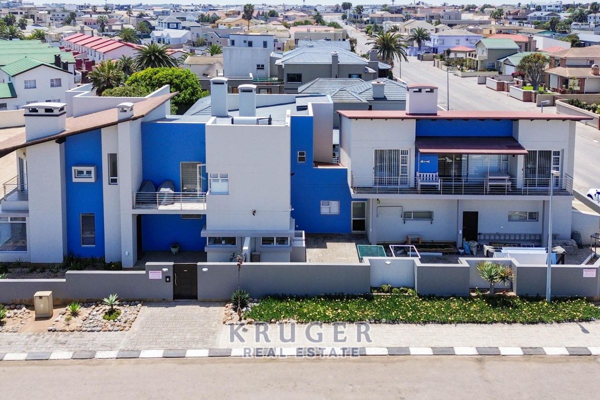 Aerial view of a modern multi-level residential property featuring blue and white exterior finishes, balconies, and a secure boundary wall with paved driveway.