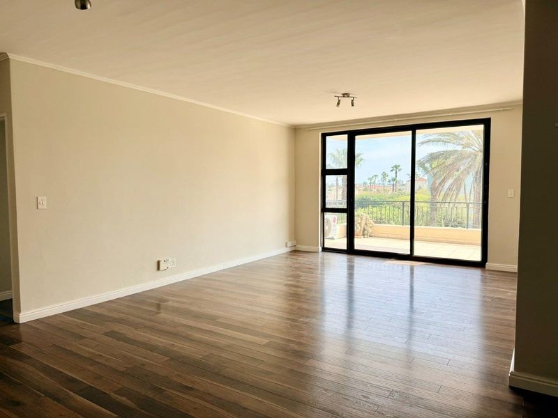 A bright and spacious empty living room featuring modern laminate flooring and large sliding glass doors leading to an outdoor balcony.