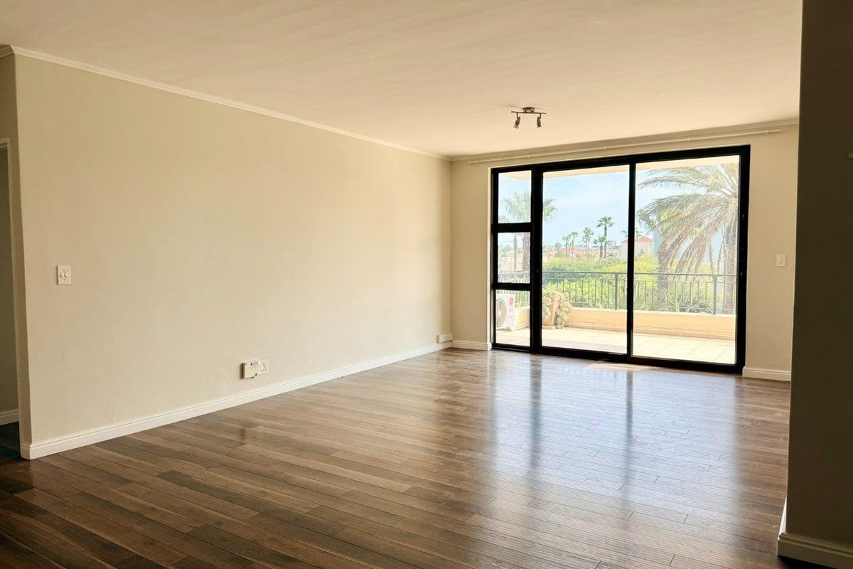 A bright and spacious empty living room featuring modern laminate flooring and large sliding glass doors leading to an outdoor balcony.