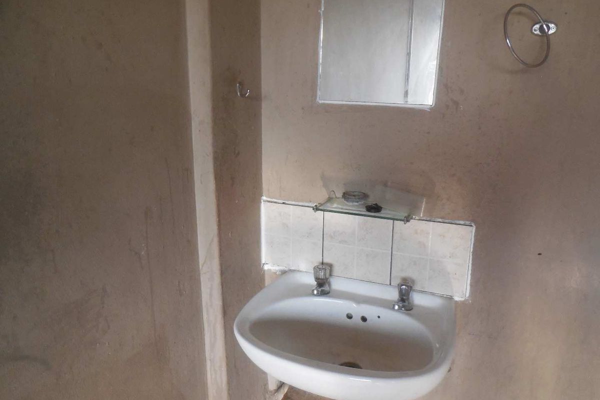 A basic bathroom vanity area featuring a wall-mounted basin, tiled splashback, and mirror, requiring cosmetic updates and wall refinishing.