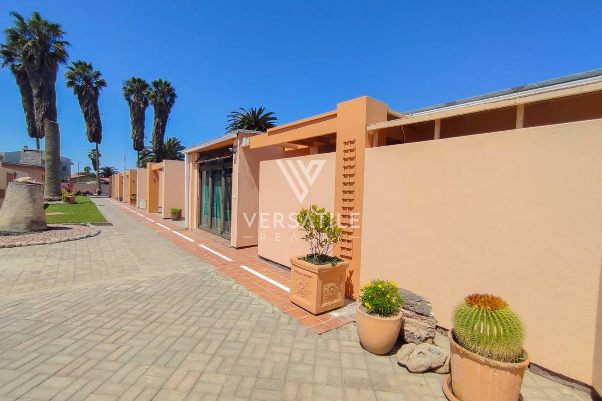Exterior view of a retirement village unit featuring a paved driveway, masonry boundary wall, and sliding glass door access.