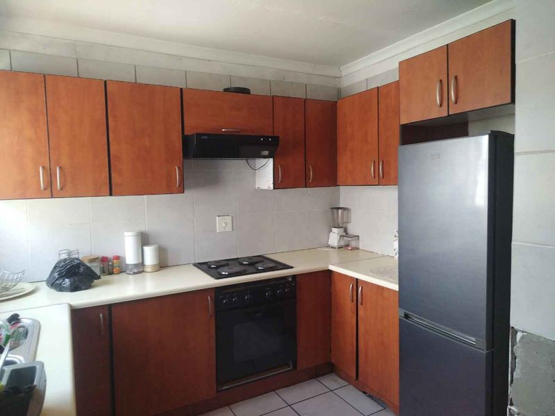 Functional kitchen featuring wood-look laminate cabinetry, built-in oven, electric hob, extractor fan, and tiled backsplash with neutral floor tiles.