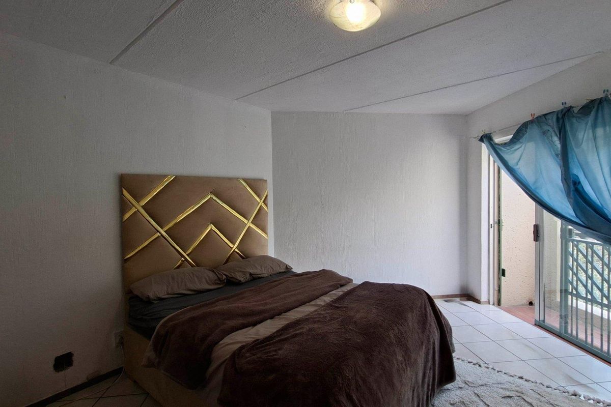 A bedroom featuring tiled flooring and a sliding glass door leading to an outdoor area, with visible ceiling damage and missing electrical outlet covers.