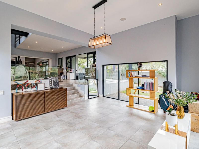 Spacious open-plan living area featuring large format floor tiles, modern pendant lighting, and seamless access to the outdoor garden through sliding glass doors.