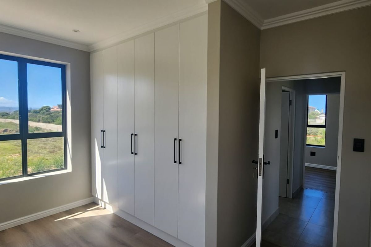 A bright bedroom featuring modern built-in cupboards, neutral wall finishes, and large windows offering scenic views.