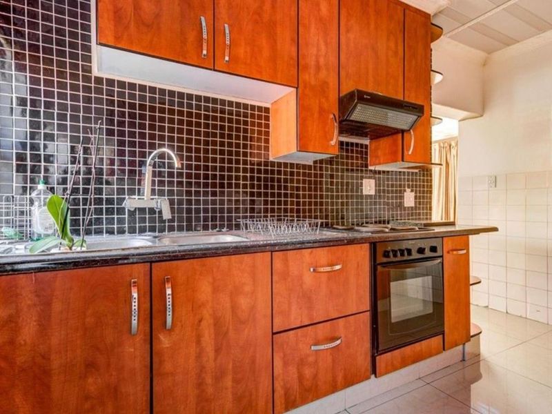 A functional kitchen featuring wood-finish cabinetry, dark tiled backsplash, integrated oven and hob, and tiled flooring.