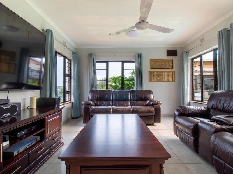A well-lit living room featuring tiled flooring, a ceiling fan, and large windows with security bars, providing a functional and comfortable living space.