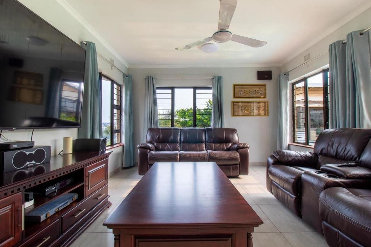 A well-lit living room featuring tiled flooring, a ceiling fan, and large windows with security bars, providing a functional and comfortable living space.