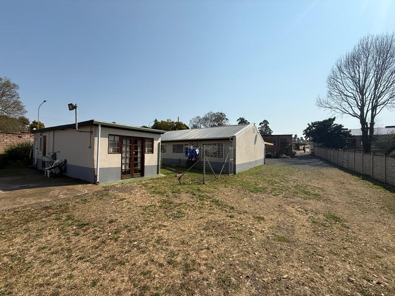 Rear view of the property showing the exterior building structure, metal roofing, and surrounding yard space with perimeter walling.