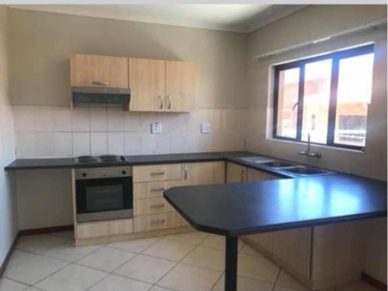 A functional kitchen featuring light wood cabinetry, dark laminate countertops, built-in oven and hob, and a double sink with tiled flooring.