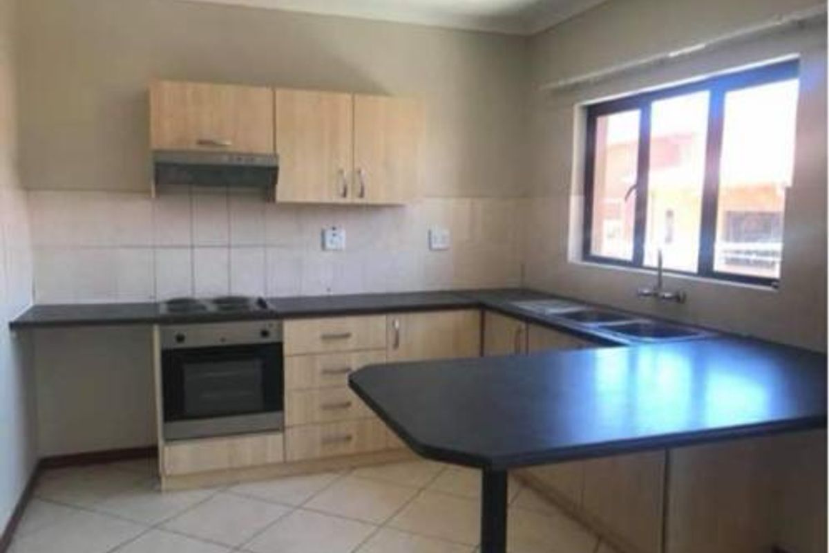A functional kitchen featuring light wood cabinetry, dark laminate countertops, built-in oven and hob, and a double sink with tiled flooring.