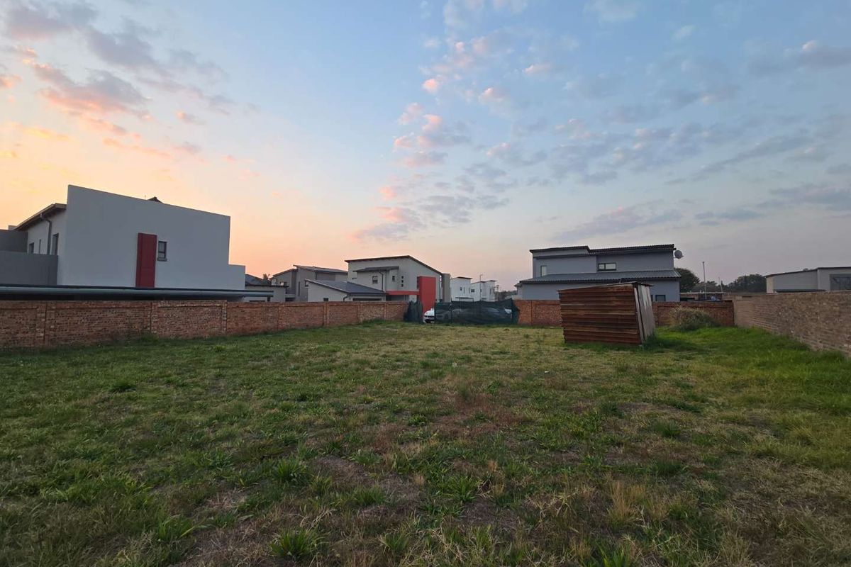A vacant residential plot featuring a grass lawn and enclosed by a brick perimeter wall, situated within a developed residential estate.