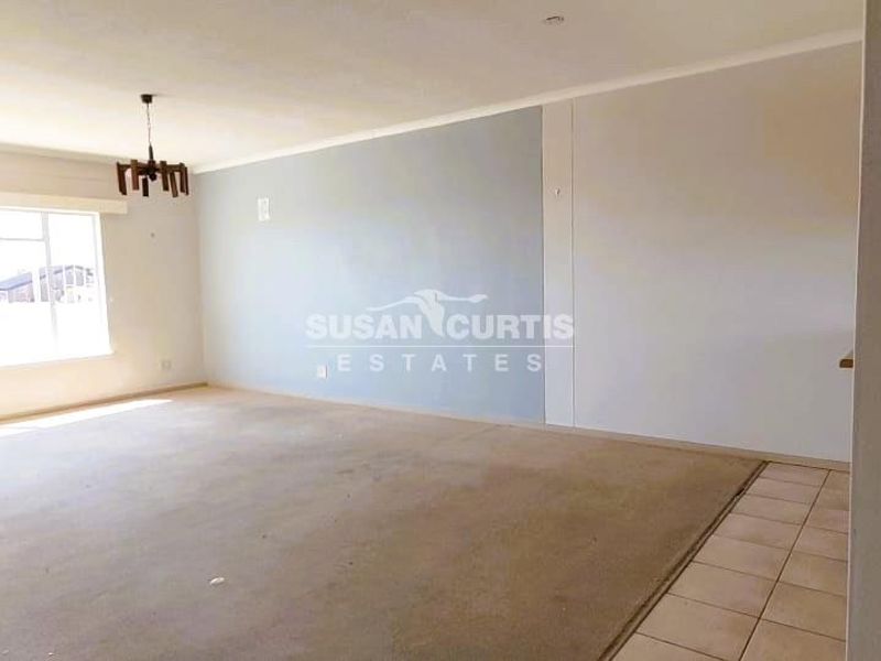 A spacious, empty living area featuring a combination of carpeted and tiled flooring, neutral walls, and a central ceiling light fixture.