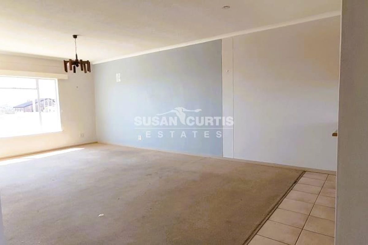 A spacious, empty living area featuring a combination of carpeted and tiled flooring, neutral walls, and a central ceiling light fixture.