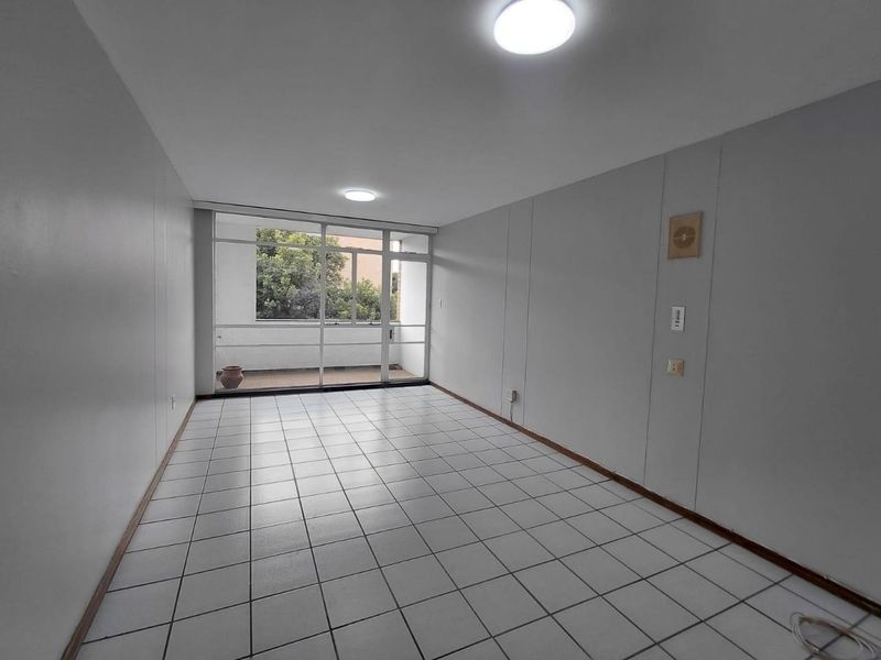 An empty, neutrally painted living area featuring tiled flooring and a large glass sliding door providing access to an outdoor balcony space.