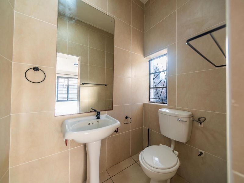 A clean, functional bathroom featuring a pedestal basin, toilet, wall-mounted mirror, and neutral floor-to-ceiling wall tiles.