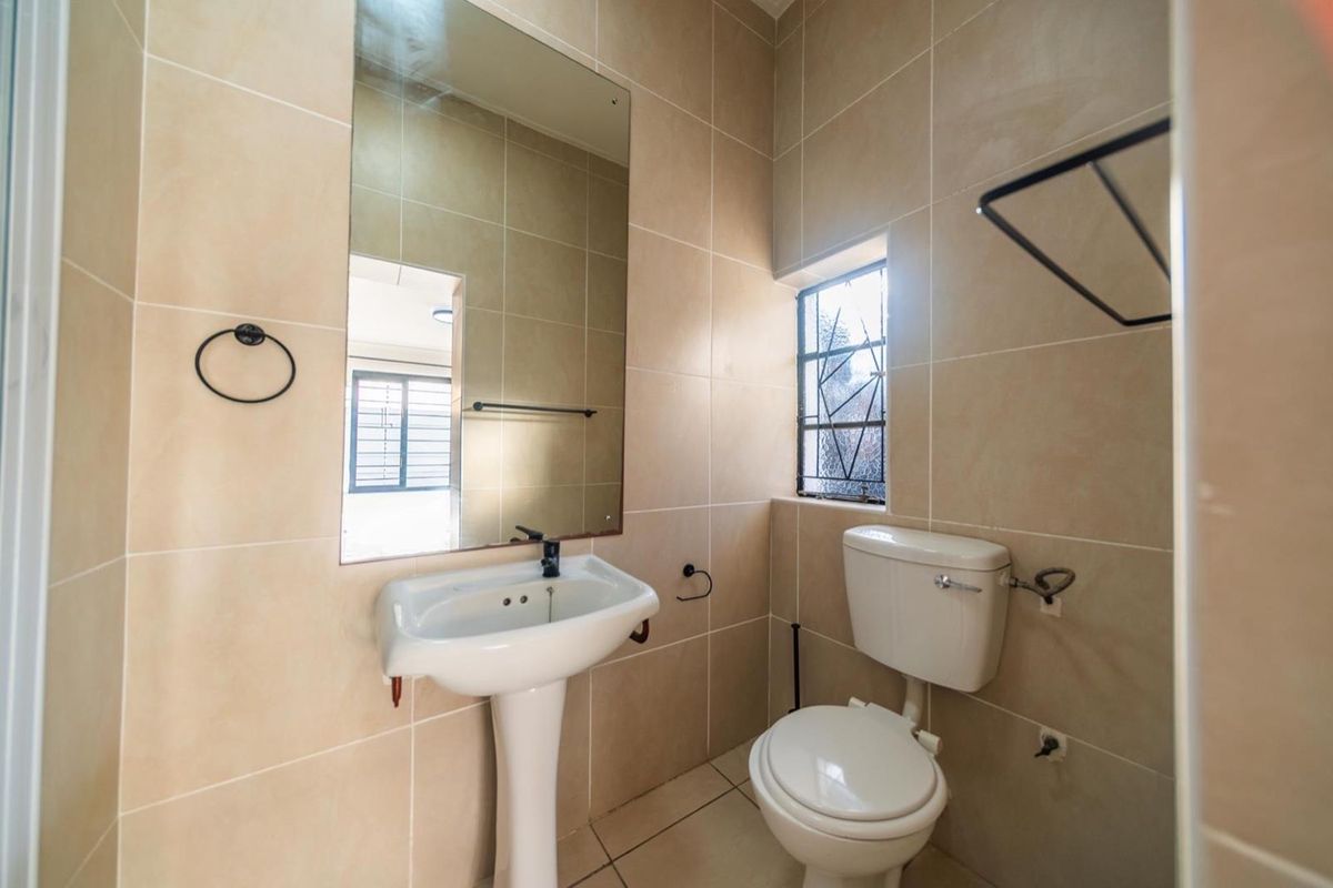A clean, functional bathroom featuring a pedestal basin, toilet, wall-mounted mirror, and neutral floor-to-ceiling wall tiles.