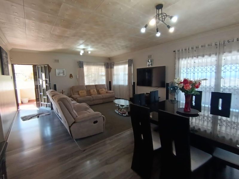 Spacious open-plan living and dining area featuring laminate flooring, textured ceilings, and direct access to an outdoor patio through a security gate.