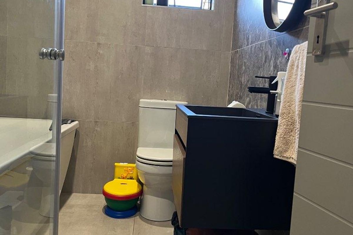 Modern bathroom featuring large format grey wall and floor tiles, a floating vanity with black basin, and a glass-enclosed shower.