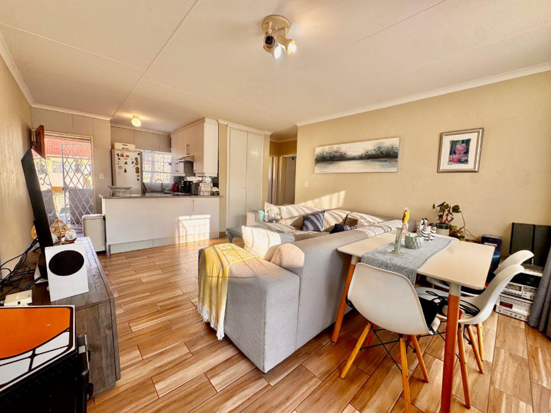 Open-plan living and dining area featuring tiled flooring, a functional kitchen with peninsula, and direct access to an exterior space via a security gate.