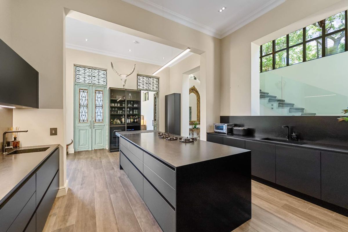 Modern kitchen featuring sleek matte black cabinetry, a central island with integrated cooktop, and high-end finishes, seamlessly connecting to the home's entrance.