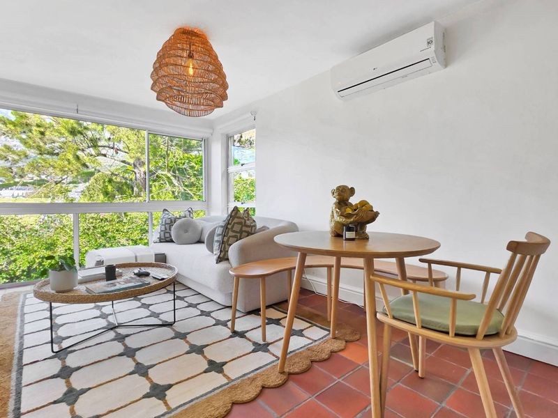 Bright living area featuring terracotta tile flooring, a wall-mounted split-system air conditioner, and large windows providing ample natural light and garden views.