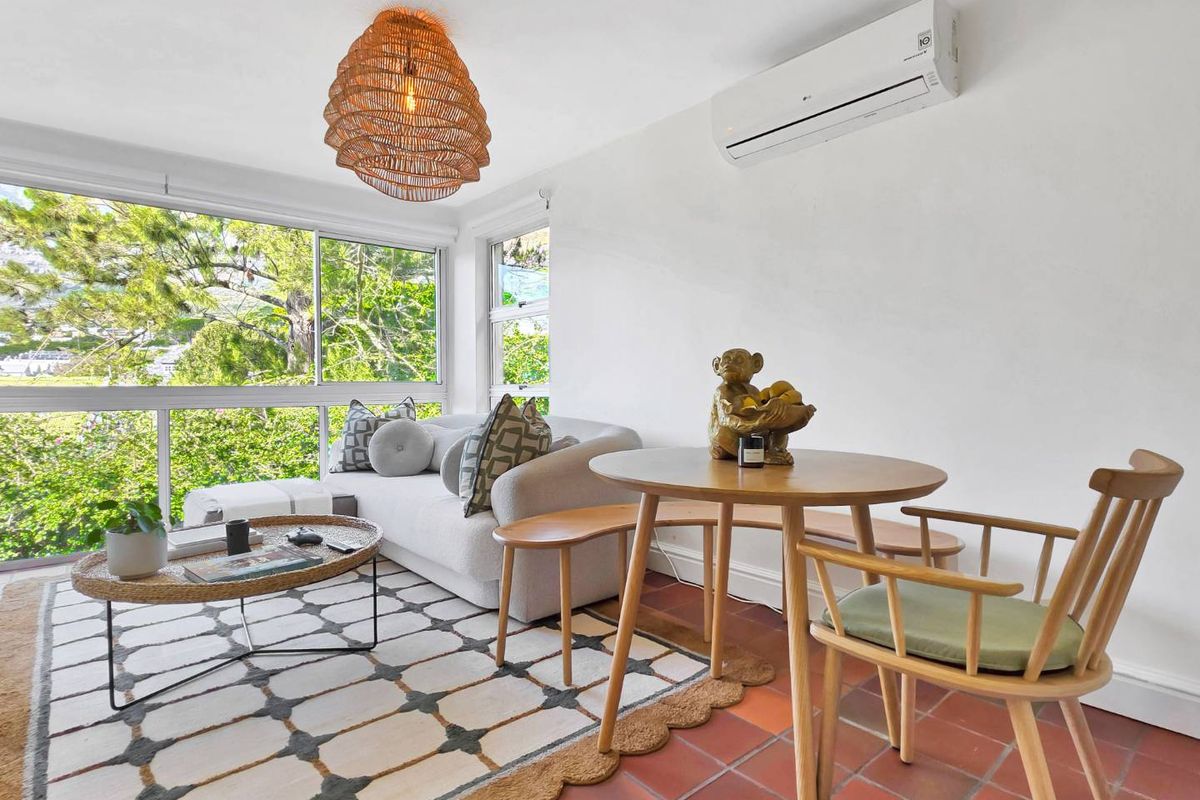 Bright living area featuring terracotta tile flooring, a wall-mounted split-system air conditioner, and large windows providing ample natural light and garden views.