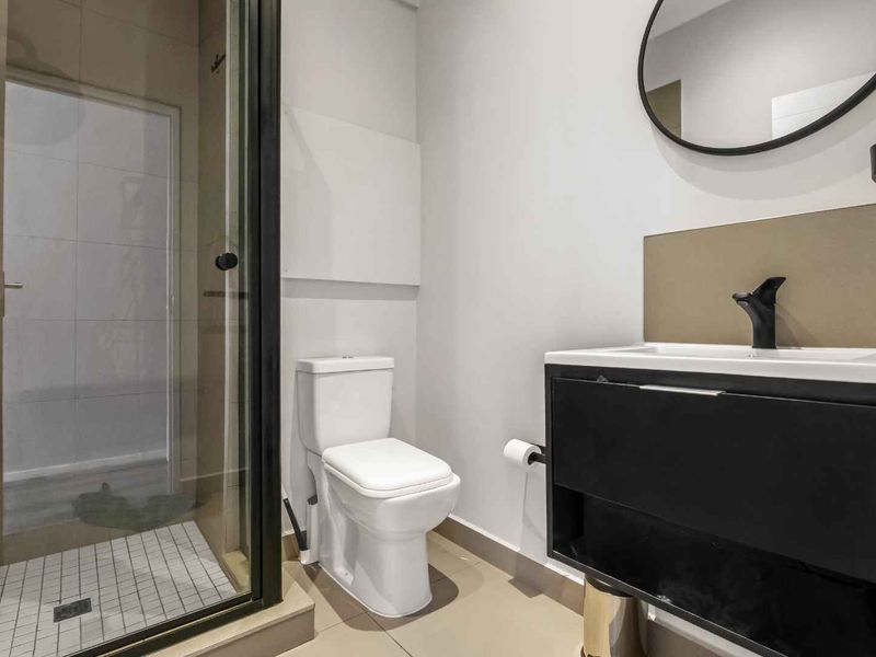 Modern bathroom featuring a glass-enclosed shower, contemporary vanity with black tapware, and neutral floor tiling.