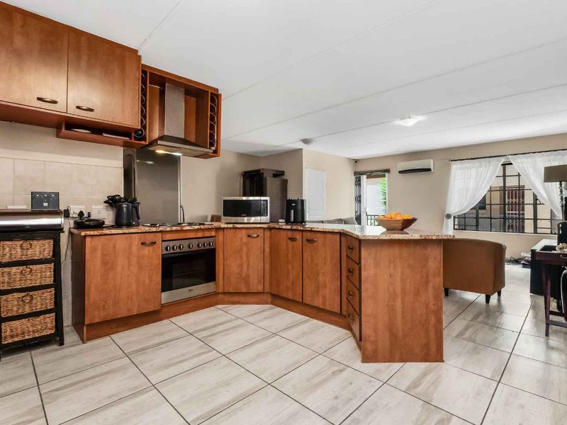 Open-plan kitchen and living area featuring wooden cabinetry, laminate countertops, built-in oven, extractor fan, and tiled flooring with access to an outdoor space.