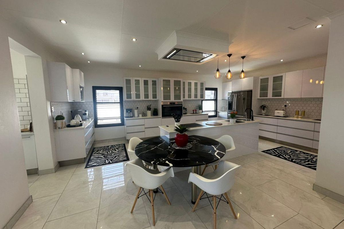 Modern, spacious kitchen featuring white cabinetry, a central island with integrated hob, high-end finishes, and sleek tiled flooring throughout.