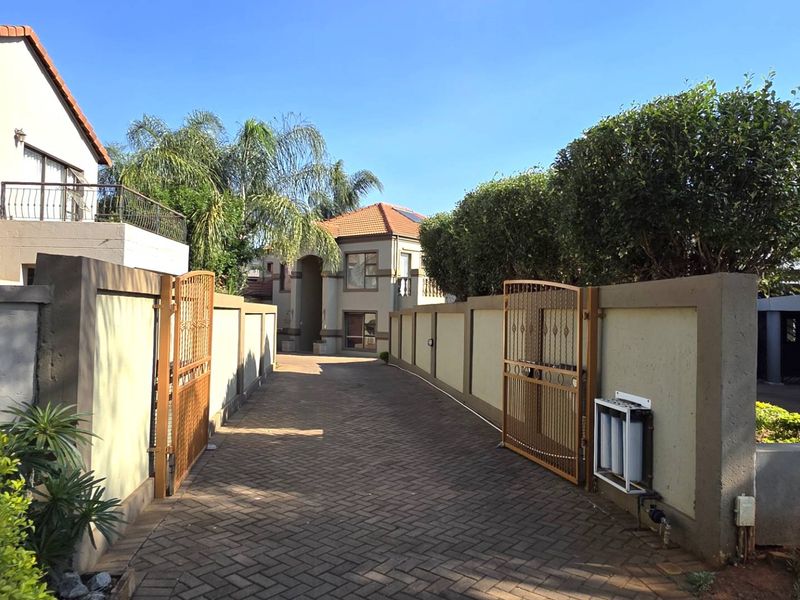 A paved driveway leading to the property entrance, featuring secure boundary walls and metal gates.