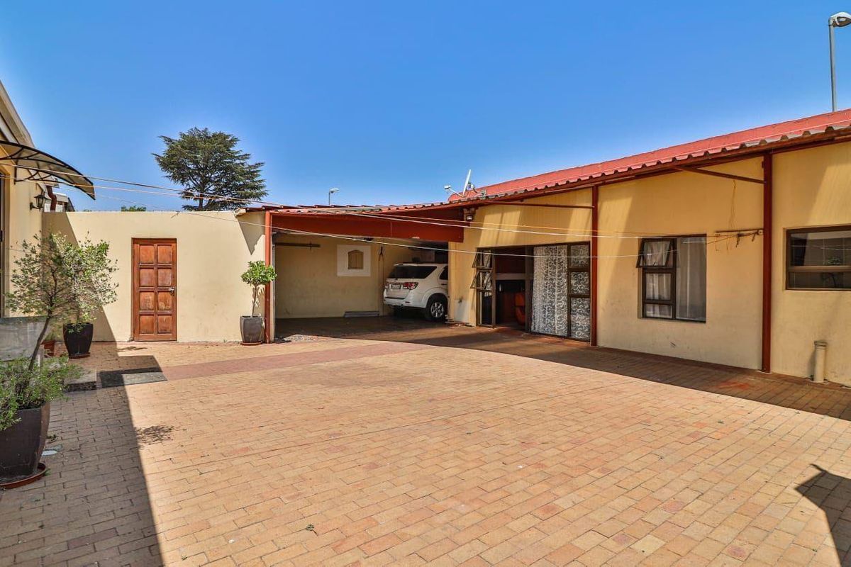 A paved rear courtyard area featuring a covered carport, brick walling, and access to the main dwelling.