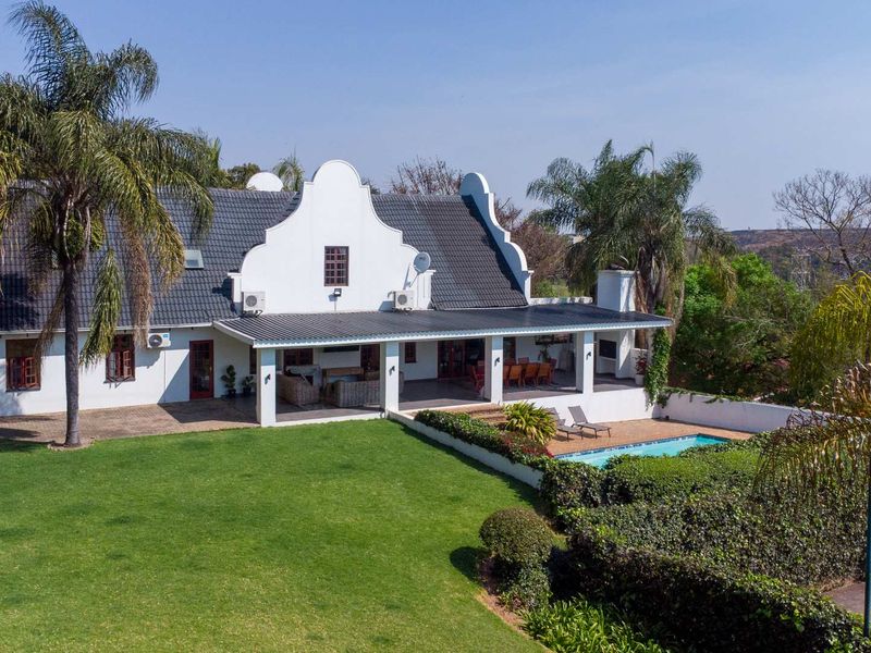 Aerial view of the rear elevation featuring a spacious covered patio, swimming pool, and well-maintained garden area with traditional gabled architecture.