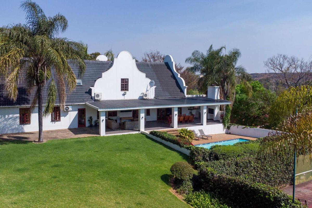 Aerial view of the rear elevation featuring a spacious covered patio, swimming pool, and well-maintained garden area with traditional gabled architecture.