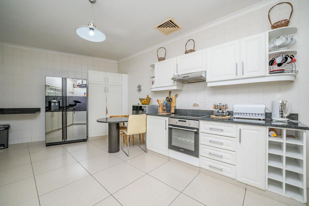 A functional kitchen featuring white cabinetry, granite countertops, built-in oven, extractor fan, and tiled flooring with ample storage space.