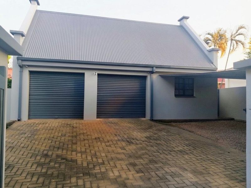 A well-maintained double garage featuring modern roller doors, a corrugated metal roof, and a paved driveway area.