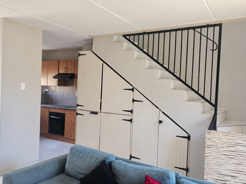Open plan living area featuring a staircase with integrated under-stair storage cabinetry and a functional kitchen with built-in oven and extractor fan.